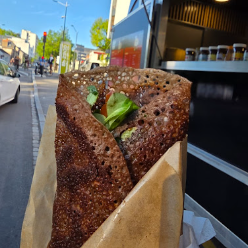 Galette de blé noir croustillante garnie, servie dans son emballage kraft devant le camion